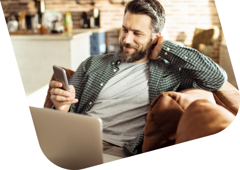 Vyras žiūri į telefoną sedėdamas ant sofos